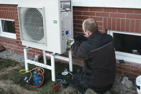 Instalator pracuje nad pompą ciepła, zapewniając jej ekonomiczne ustawienie. Widać narzędzia i sprzęt do montażu.