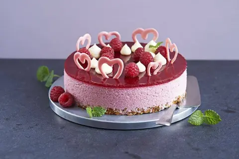 En vacker hallonmousse tårta med färska hallon och rosa hjärtdekorationer, perfekt för ett speciellt tillfälle.
