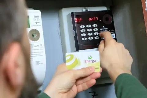 Osoba dokonuje doładowanie licznika przedpłatowego, wprowadzając kod na klawiaturze i trzymając kartę Energa.