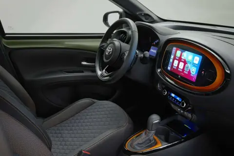 Interni moderni della Toyota Aygo X: sedili trapuntati, volante sportivo e un vivace touchscreen centrale con Apple CarPlay.