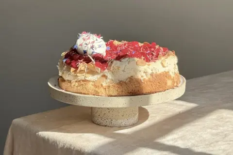 Eine köstliche Sommer Torte mit Baiserhaube, roten Beeren und Mandelsplittern, verziert mit essbaren Blüten.