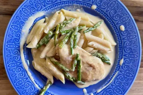 Penne z piersią kurczaka i szparagami w kremowym sosie, podane na niebieskim talerzu.