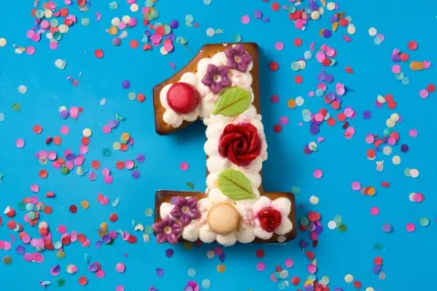 Ein süßer number cake in Form einer Eins, verziert mit Sahne, Blumen und Rosen, umgeben von buntem Konfetti.