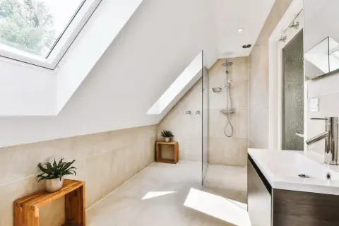 Salle de bain sous pente avec douche à faible hauteur, lavabo moderne et puits de lumière.