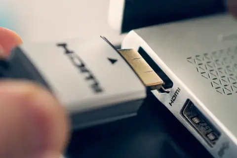 Ein Finger steckt ein HDMI-Kabel in den HDMI-Anschluss eines Laptops.