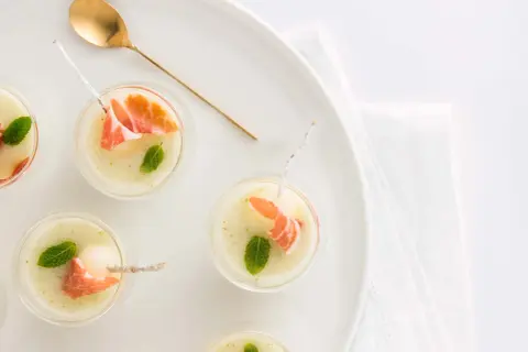 Delicioso chupito de melón con jamón serrano y menta, servido en copas pequeñas con una cuchara dorada.