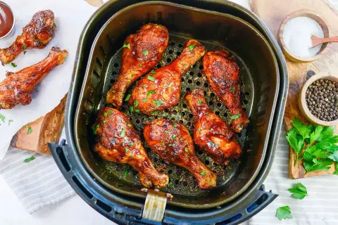 Soczyste udka z kurczaka z airfryer, polane sosem barbecue i posypane natką pietruszki. Obok miseczki z solą i pieprzem.