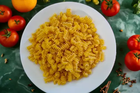 Ein Teller mit gedrehten Nudeln, die aus Hartweizengrieß hergestellt sind, umgeben von frischen Tomaten und Gewürzen.