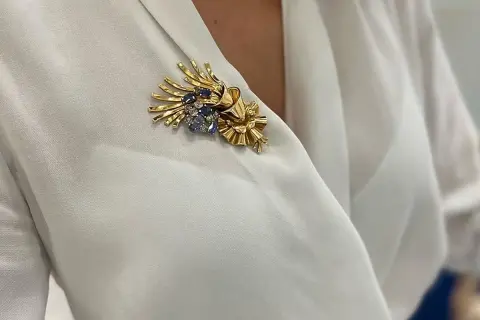 Una joya en forma de broche de oro con zafiros y diamantes, adornando una blusa blanca.