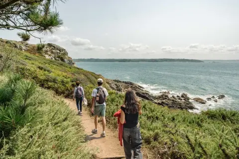 Trois randonneurs explorent un sentier côtier verdoyant, le **gr 34**, face à la mer d'un bleu profond.