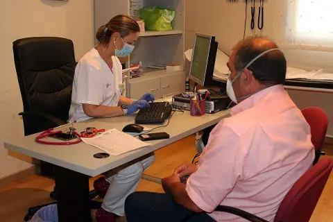 Enfermera con mascarilla atiende a paciente con mascarilla, tramitando un hospital justificante médico urgencias.