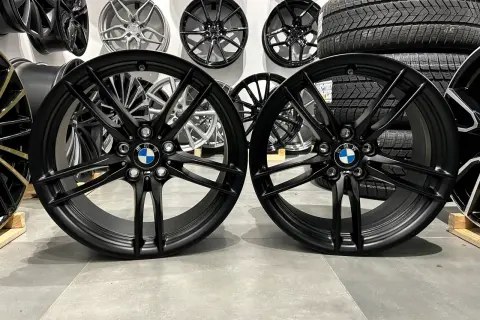 Dwa czarne felgi BMW z logo, idealne do tuningu. W tle inne felgi i opony.