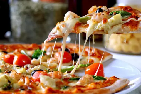 Rozciągający się ser z kawałka pizzy z krewetkami, pomidorkami i oliwkami. To jeden z wielu pysznych rodzajów pizzy włoskiej.