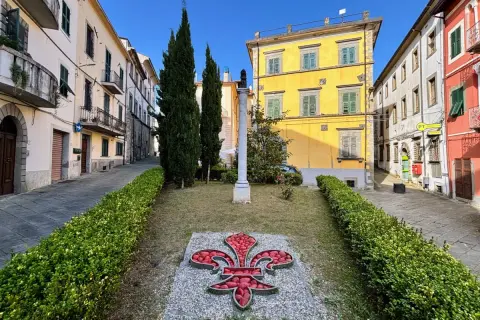 Fivizzano cosa vedere: un'aiuola con un giglio rosso e un monumento in un vicolo con case colorate.