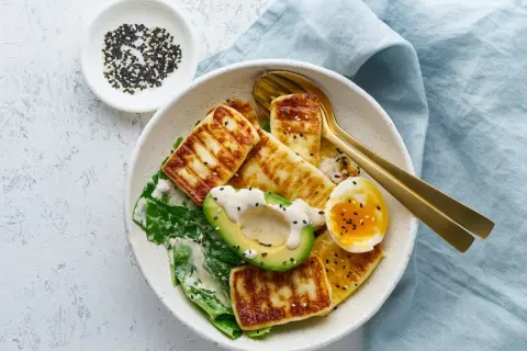 Sałatka z grillowanym serem halloumi, awokado, jajkiem i zielonymi liśćmi, posypana sezamem.