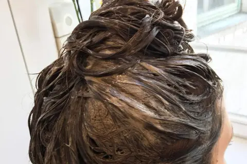 Dunkelbraunes Haar mit Farbauftrag, das auf die Einwirkzeit wartet. Wie lange muss Farbe beim Friseur einwirken?