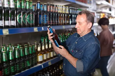 Mężczyzna w dżinsowej koszuli wybiera piwo w sklepie. Zastanawia się, ile kosztuje piwo w Polsce, przeglądając bogaty asortyment.