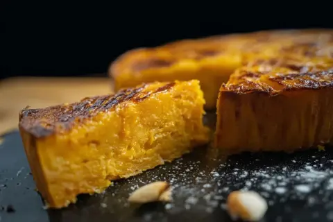 Un morceau de gâteau patate douce, doré et moelleux, est présenté sur une assiette noire saupoudrée de sucre glace.