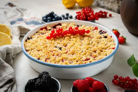 Ein köstlicher Beeren Crumble mit roten Johannisbeeren, Blaubeeren und Himbeeren, garniert mit frischen Beeren und Zitronenspalten.