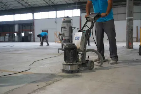 Trabajadores pulen un suelo de hormigón con una máquina. Se muestra cómo hacer hormigón para suelo, preparando la superficie.