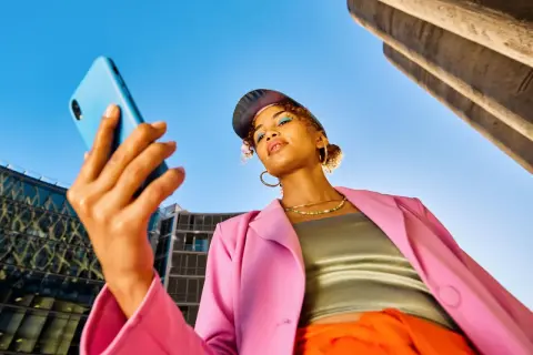Junge Frau mit Handy in der Hand, blickt nachdenklich. Ist Influencer ein Beruf? Sie inspiriert mit ihrem Style.