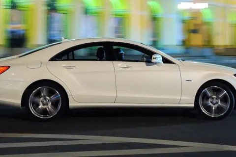Biały Mercedes CLS 63 AMG mija nocą rozmyte światła miasta, jego sylwetka jest dynamiczna i elegancka.