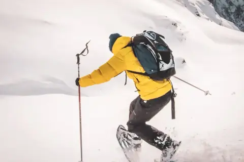 Une personne en raquettes, veste jaune, sac à dos, profite d'une rando raquette Vosges dans un paysage enneigé.