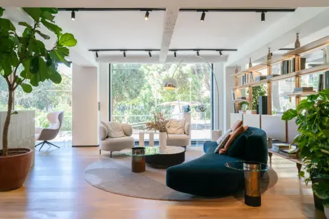Amplio salón con sofás curvos, sillones, mesas de centro y estanterías, todo bañado por luz natural a través de grandes ventanas modernas.