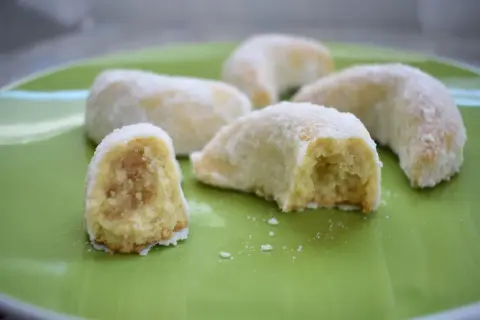 Petits gâteaux en forme de croissant, saupoudrés de sucre glace. Ces délices ressemblent à des cornes de gazelle, prêts à être dégustés.
