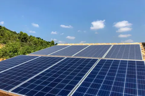 Mi experiencia con placas solares: paneles azules captan la luz del sol en un tejado, con colinas verdes y cielo azul de fondo.