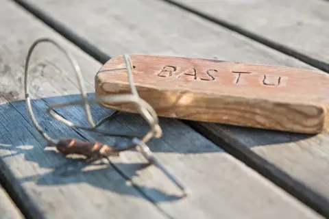 En träbit med texten "BASTU" och en metallskopa ligger på en träbrygga. Kanske en påminnelse om en härlig stund på Östholmen bastu.