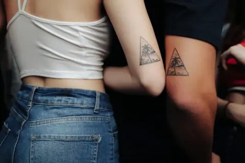 Zwei Arme mit passenden Dreiecks-Tattoos, die Palmen und eine Hängematte zeigen. Eine schöne Tattoo Idee Familie, die Verbundenheit symbolisiert.