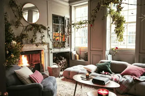 Acogedor salón decorado de Navidad con chimenea encendida, árbol y guirnaldas verdes colgando.