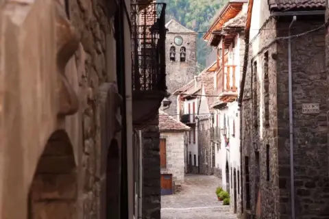 Calle empedrada en un pueblo de Aragón, con casas de piedra y un campanario al fondo.