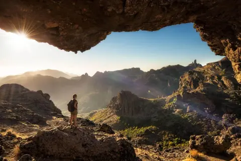 Una persona con mochila admira el paisaje montañoso al amanecer, disfrutando de unas increíbles caminatas Gran Canaria.
