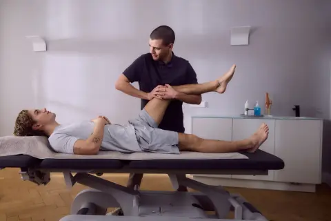 Physiotherapeut führt krankengymnastik hws durch, indem er das Bein eines liegenden Patienten sanft bewegt.