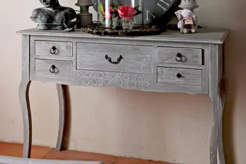 Console grise patinée, ornée de motifs floraux sculptés. Ce meuble à tiroirs, idéal pour un intérieur cosy, invite à y poser des objets décoratifs.