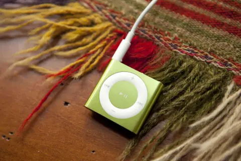 A green iPod Shuffle, a relic from when MP3 players were invented, rests on a wooden surface next to a colorful, fringed scarf.