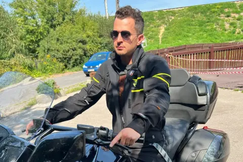 Mężczyzna w okularach przeciwsłonecznych i czarnej kurtce motocyklowej, gotowy na podróż.