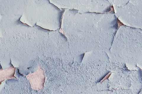 Texture d'un plafond avec peinture écaillée, révélant la couche inférieure rosée. Les craquelures créent un motif abstrait.