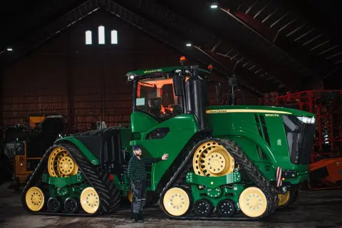 Man bredvid en stor grön John Deere-traktor i en lada. Frågan "hur länge håller diesel" kan vara relevant för denna maskin.