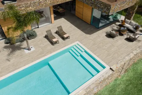 Una piscina azzurra e una moderna pavimentazione esterna in legno creano un'oasi di relax con arredi da esterno e una palma.