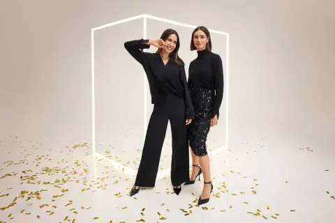 Dwie kobiety w eleganckich czarnych strojach, jedna w spodniach, druga w cekinowej spódnicy. Gerry Weber sukienki i stylizacje na wyjątkowe okazje.