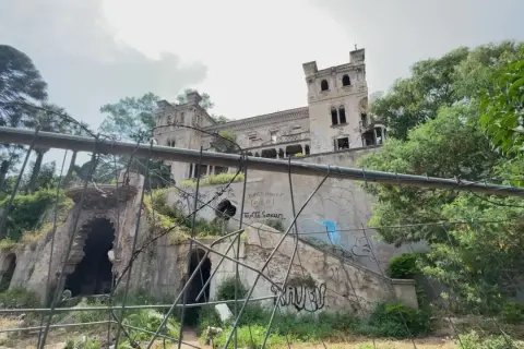 Ruines d'un château délabré, envahi par la végétation et couvert de graffitis. Un portail orné et des tours menacent de s'effondrer. Une scène d'urbex flippant.