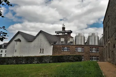 Edificio della Brasserie du Bocq con serbatoi in acciaio inox e un cielo nuvoloso.