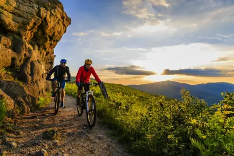 Dwóch rowerzystów na szlaku górskim podczas zachodu słońca. To idealny przykład turystyki rowerowej w Polsce.