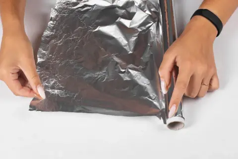 Dłonie rozwijają folię aluminiową, by zapobiec powstawaniu kożucha na sosie. Jak go zabezpieczyć folią?