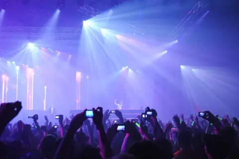 Tłumy na rave festivalu filmują DJ-a na scenie oświetlonej laserami.