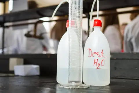Bouteilles d'eau distillée et éprouvette graduée sur un établi de laboratoire, prêtes pour la stérilisation eau chaude.