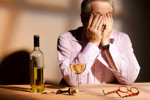Mann mit Händen vor dem Gesicht, Wein, Korkenzieher und Brille auf dem Tisch. Ein Bild, das die Verzweiflung und die Folgen von Korsakow-Syndrom symbolisiert.